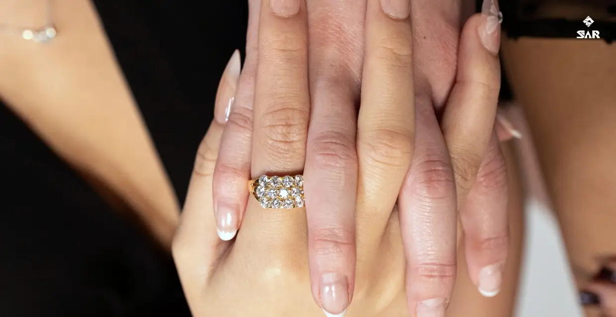 Stacked hands wearing a yellow-gold pavé band with white-gold and rose-gold tennis bracelets