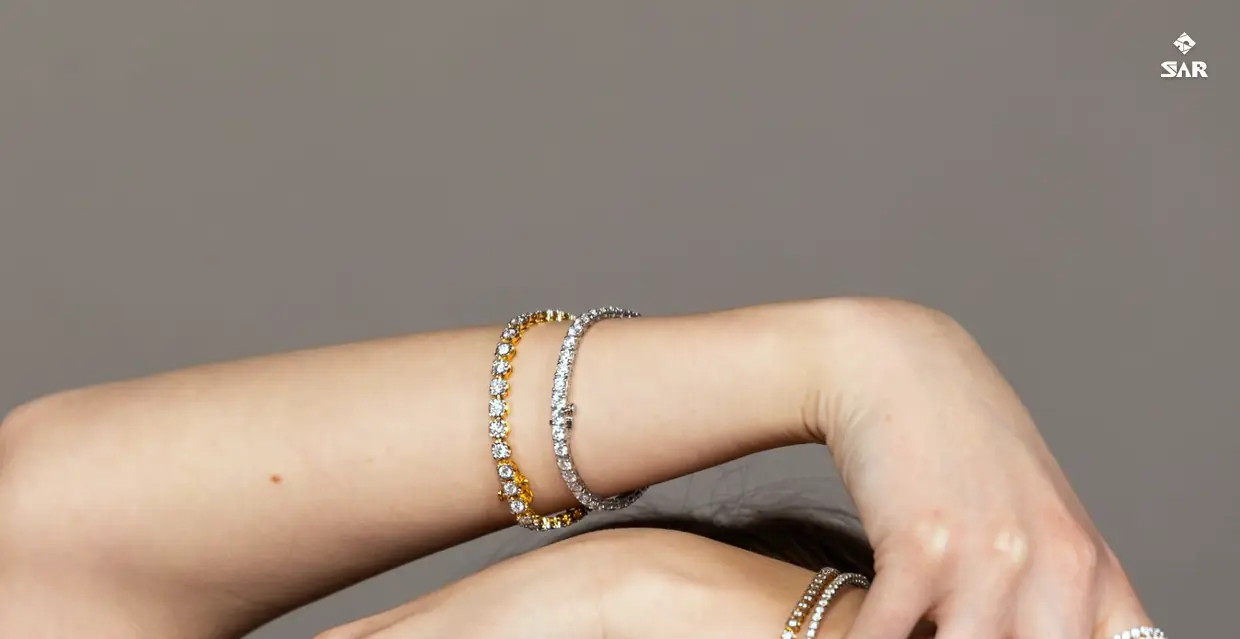 A model with her arms raised, wearing tennis bracelets, diamond rings, a stud earring and a tennis necklace