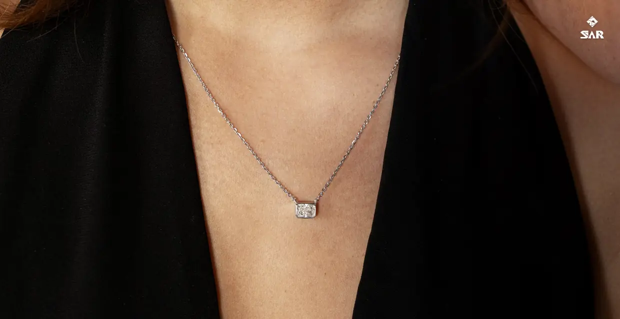 A radiant-cut lab-grown diamond in a bezel pendant on a fine chain, worn with a black top